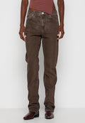 Person in gerad geschnittenen braunen Jeans, dunkelbraunen Lederstiefeln und einem asymmetrischen mauvefarbenen Oberteil vor einem schlichten hellen Hintergrund.