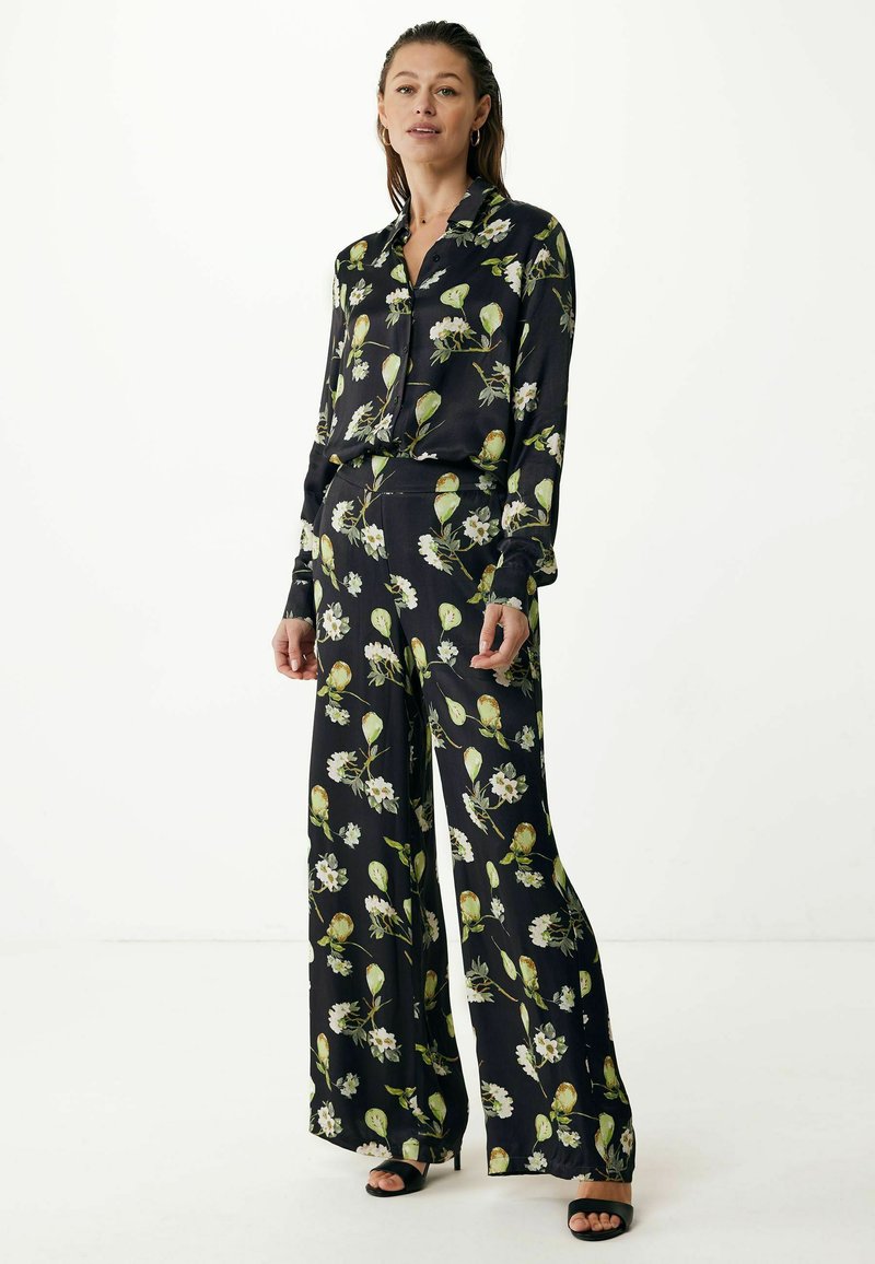 Schwarz gemusterte Bluse mit Blumenmotiven und weit geschnittene Hose aus weichem Stoff mit grünen und weißen Blumenmustern. Mit einem kragenförmigen Ausschnitt und langen Ärmeln.