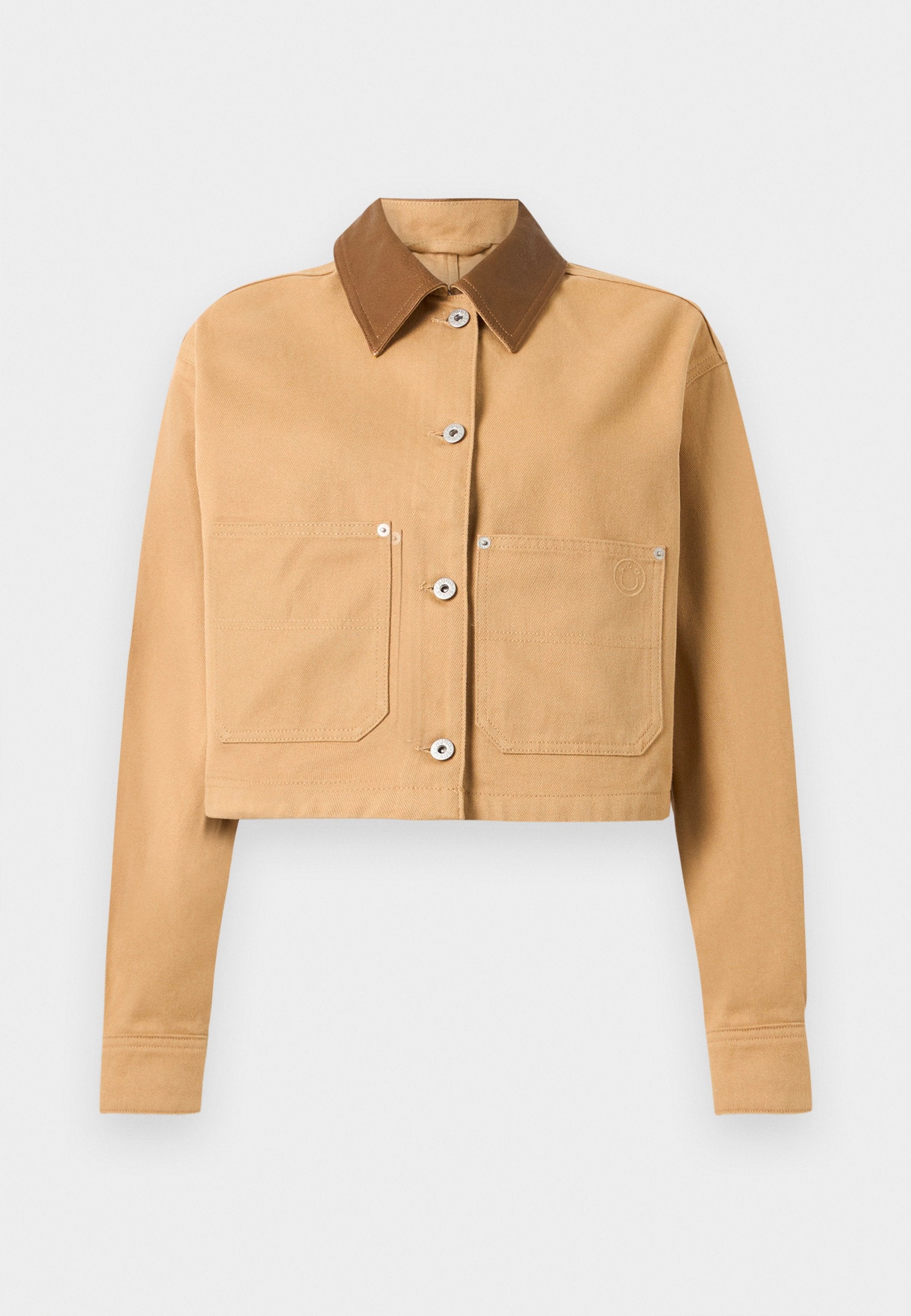 Abgeschnittene beige Jacke mit langen Ärmeln, zwei Fronttaschen, silbernen Knöpfen und einem dunkler braunen Spitzkragen auf weißem Hintergrund.