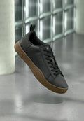 Schwarze Leder-Sneaker mit strukturierter Rückseite, brauner Gummisohle, abgerundeter Zehenpartie und flachen Schnürsenkeln; mit seitlichen Perforationen für Atmungsaktivität.
