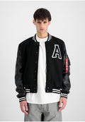 Schwarze Varsity-Jacke mit Lederärmeln, weiß gestreiftem, geripptem Kragen und Bündchen, großem "A"-Patch auf der Brust und rotem Etikett detail am Ärmel.
