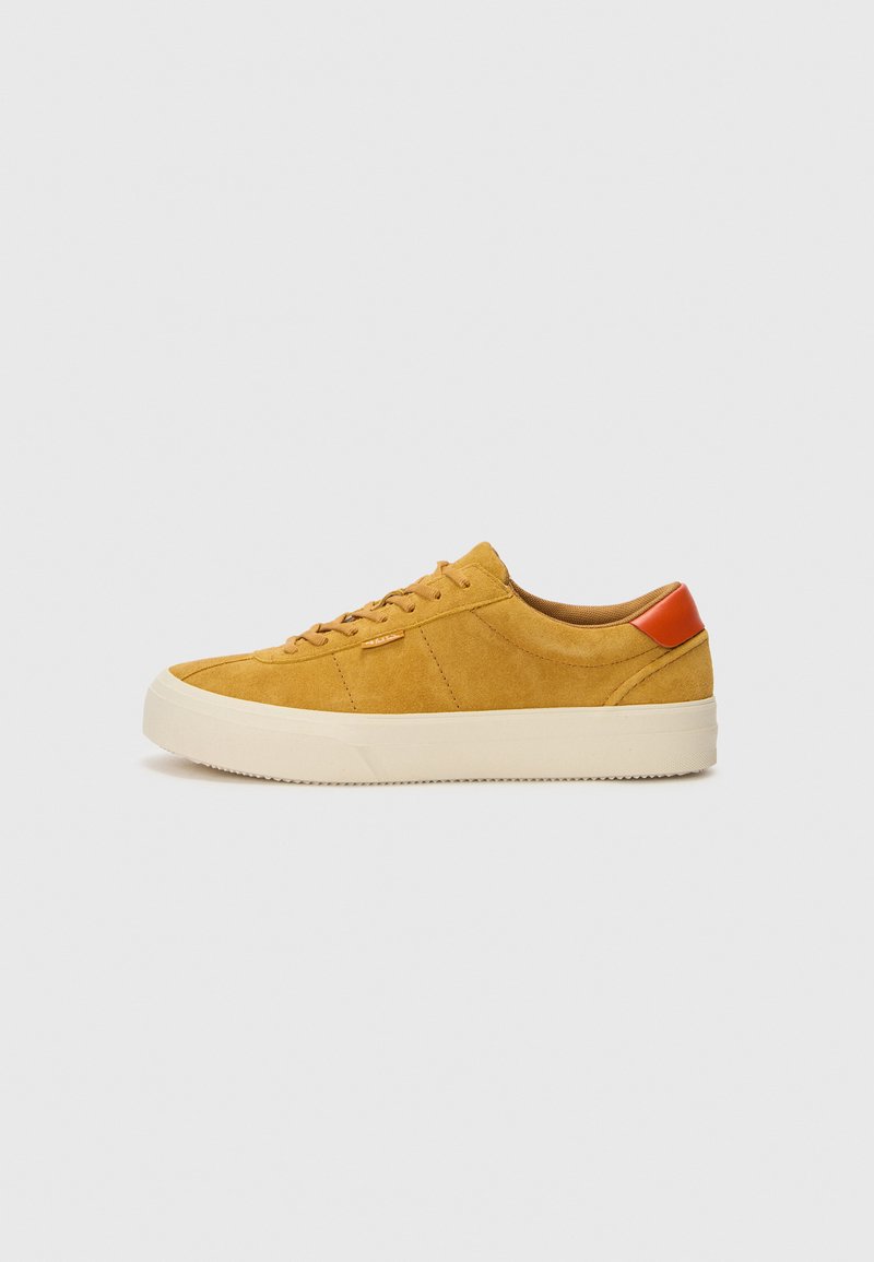 Gelbe Wildlederschuhe mit einer cremigen Gummisohle, versehen mit braunen Akzenten und Schnürdesign, strukturierten Oberflächen und seitlichen Stickdetails.
