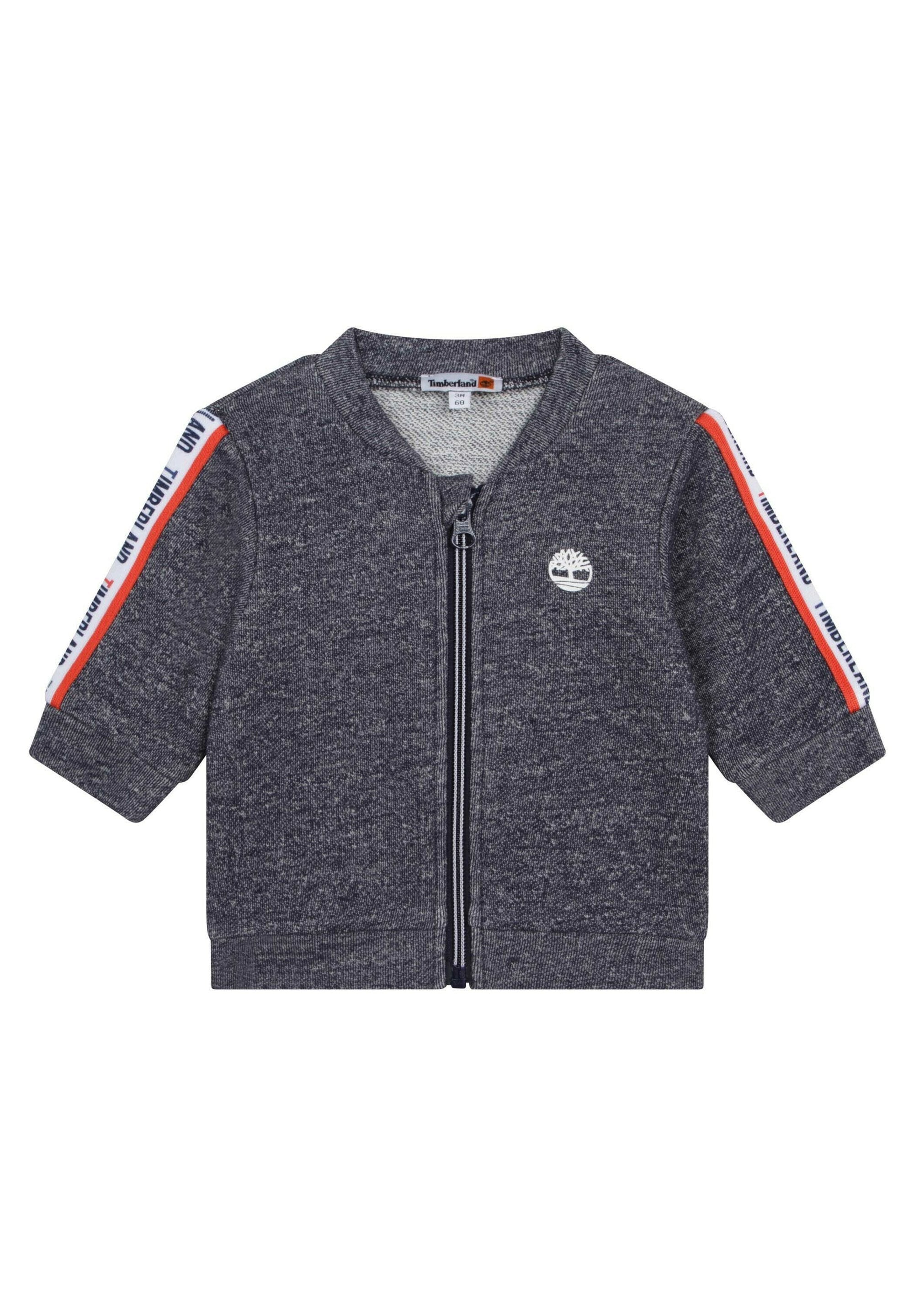 Dunkelgraue Zip-Jacke mit kurzen Ärmeln, die ein weißes Logo auf der Brust und rot-blaue gestreifte Akzente an den Schultern aufweist.