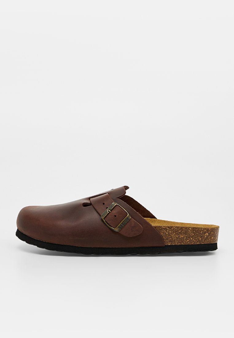 Brauner Lederschlupfschuh mit verstellbarem Schnallenriemen und Korkfußbett, schwarze Sohle, isoliert auf weißem Hintergrund.