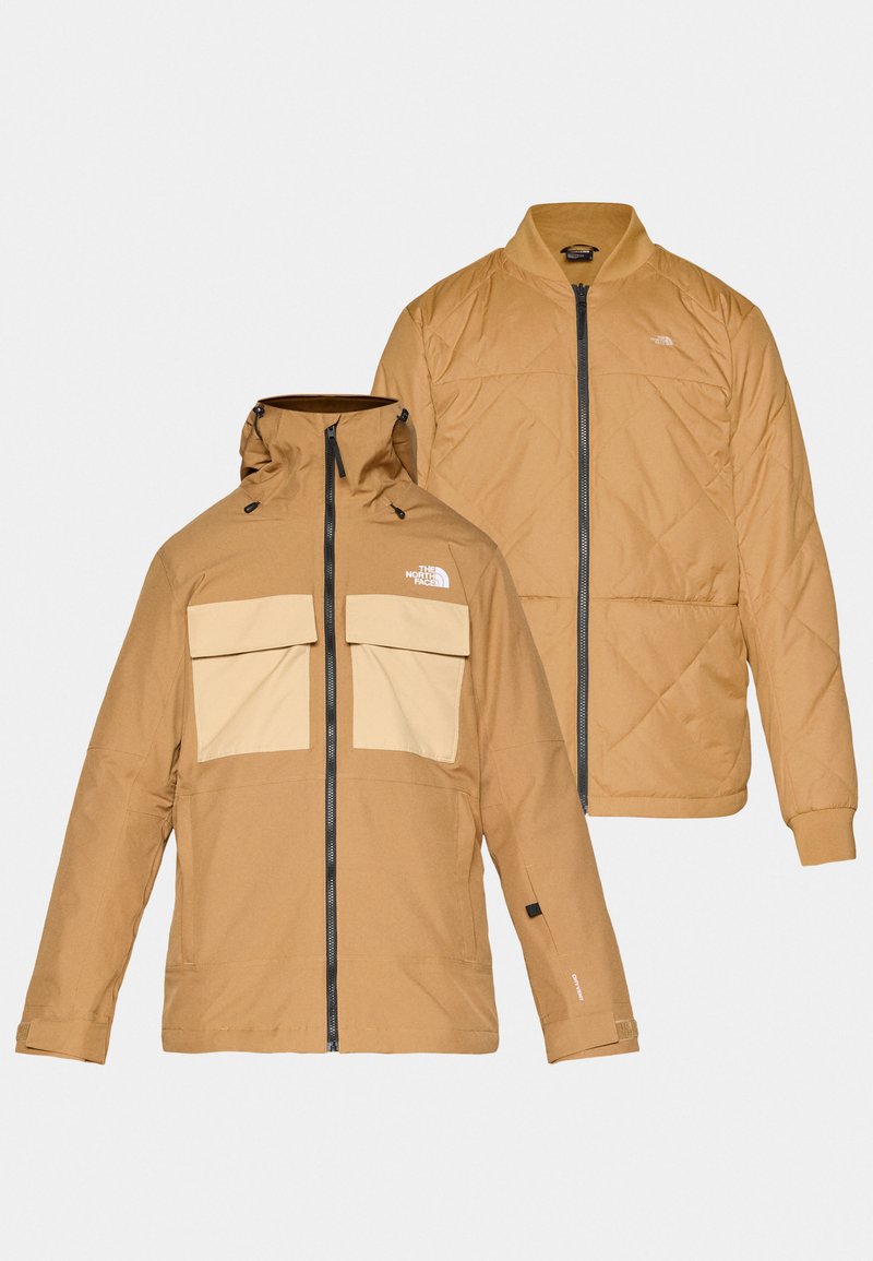 Braune Outdoor-Jacke mit abnehmbarem Kapuze und zwei großen Fronttaschen. Das Innere hat ein gestepptes Design in einer ähnlichen Farbe.