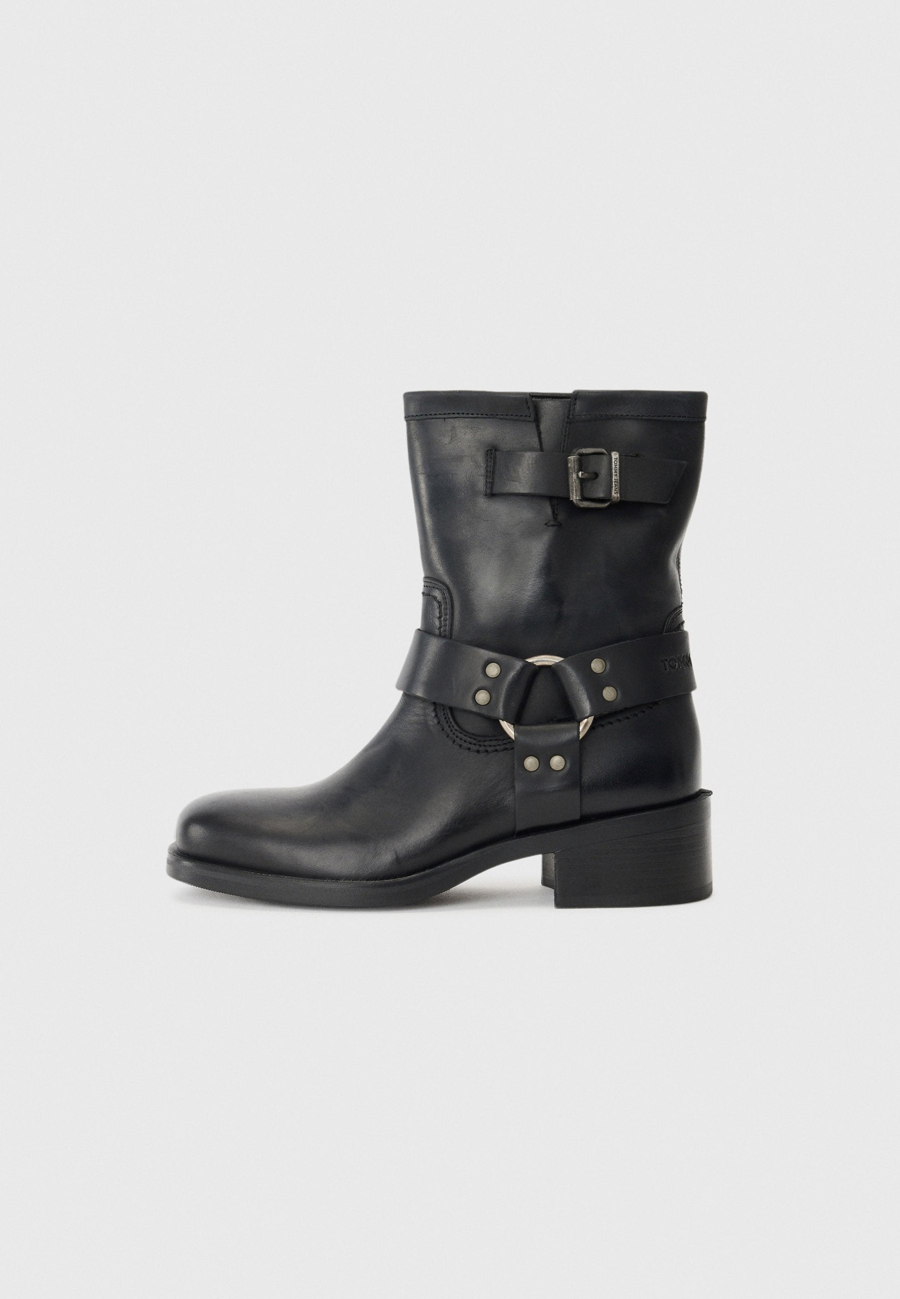 Schwarze Lederknöchelstiefel mit einem massiven Absatz, ausgestattet mit einem Riemen und einem runden Hardware-Detail sowie einer Schnallenakzentierung im oberen Bereich.