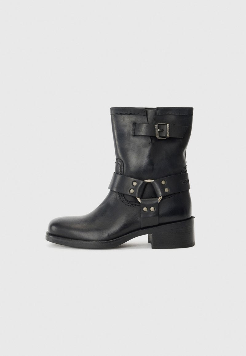 Schwarze Lederknöchelstiefel mit einem massiven Absatz, ausgestattet mit einem Riemen und einem runden Hardware-Detail sowie einer Schnallenakzentierung im oberen Bereich.