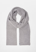 Hellgrauer, gestrickter Wollschal mit geripptem Muster, zu einer Schlaufe gelegt, Enden hängen herab, kleines Markenschild an einem Ende sichtbar.