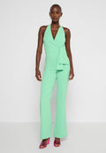 Mintgrüner Halter-Jumpsuit mit Wickeldesign, ausgestattet mit einem Knoten in der Taille und ausgestellten Beinen. Das Model trägt pinke Absätze. Glatte, enganliegende Textur.