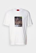 Weißes Baumwoll-T-Shirt mit einem rechteckigen Grafikdruck und dem Schriftzug "HUGO" auf einer strukturierten, dunklen Oberfläche, umgeben von Grünpflanzen.