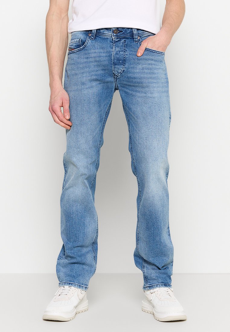 Helle blaue Jeans aus Denim mit geradem Schnitt, Fünf-Taschen-Design und kontrastierenden Nähten. Getragen mit weißen Turnschuhen.