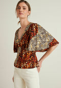 Bunt gemusterte Bluse mit V-Ausschnitt, weiten Ärmeln und einer Kombination aus Leoparden- und Tierdruckmustern in Rot, Schwarz, Gelb und Beige.