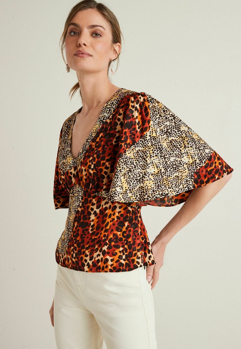 Bunt gemusterte Bluse mit V-Ausschnitt, weiten Ärmeln und einer Kombination aus Leoparden- und Tierdruckmustern in Rot, Schwarz, Gelb und Beige.