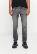 Mann in schmal geschnittenen grauen Jeans und schwarzen Sneakers vor einem weißen Hintergrund, stehend mit entspannten Händen an den Seiten.