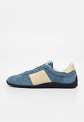 Blauer Wildleder-Sneaker mit beiger Seitenpartie, schwarzer Sohle und Schnürdesign, von der Seite auf weißem Hintergrund gezeigt.