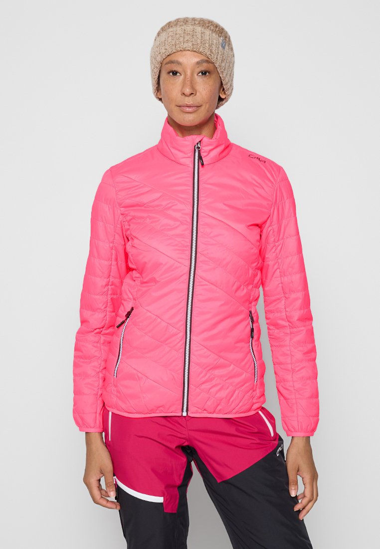 Heller rosa isolierter Jacke mit hohem Kragen, Reißverschluss und diagonalen Nähten. Kombiniert mit dunklen Hosen, die weiße Akzente aufweisen.