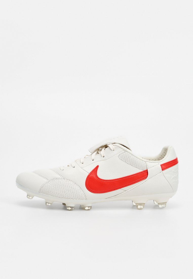 Weißer Fußball-Schuh mit rotem Nike-Swoosh und Nocken auf der Sohle, seitlich auf schlichtem Hintergrund dargestellt.