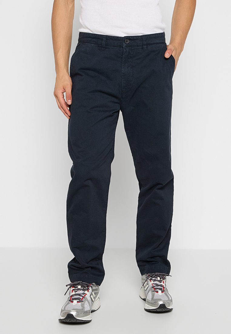 Marineblaue Chinos aus Baumwollmix, mit einem Knopfverschluss, gerader Beinform und Seitentaschen. Getragen mit grauen Sportschuhen.