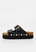 Schwarze Slip-On-Sandale mit Korkfußbett, dicker schwarzer Sohle, zwei verstellbaren Riemen mit goldenen Schnallen und dekorativen goldenen Nieten an der Seite.