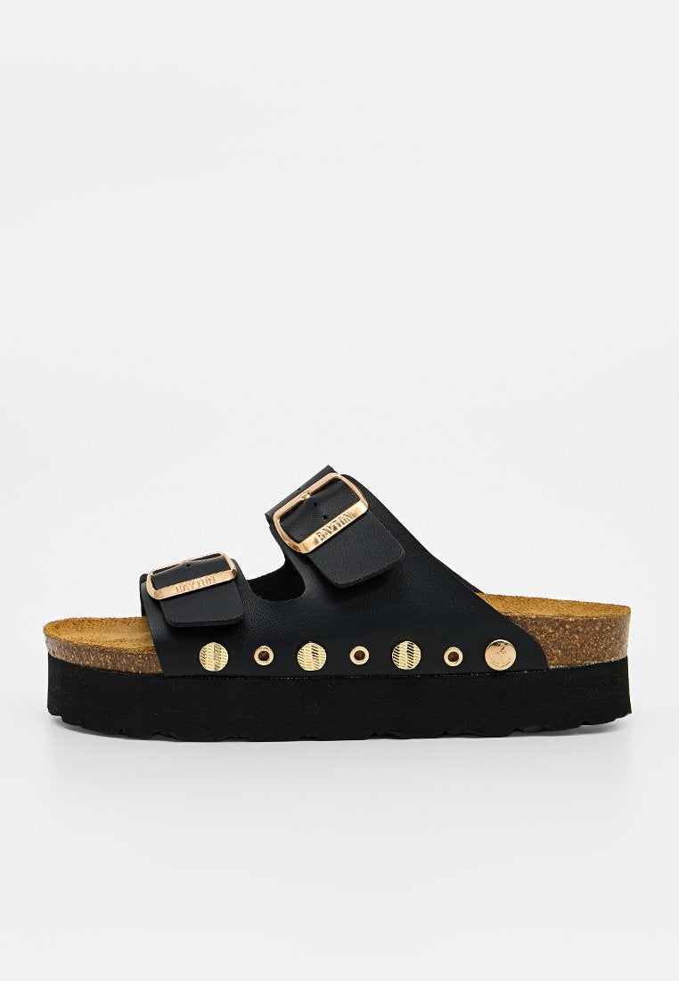 Schwarze Slip-On-Sandale mit Korkfußbett, dicker schwarzer Sohle, zwei verstellbaren Riemen mit goldenen Schnallen und dekorativen goldenen Nieten an der Seite.