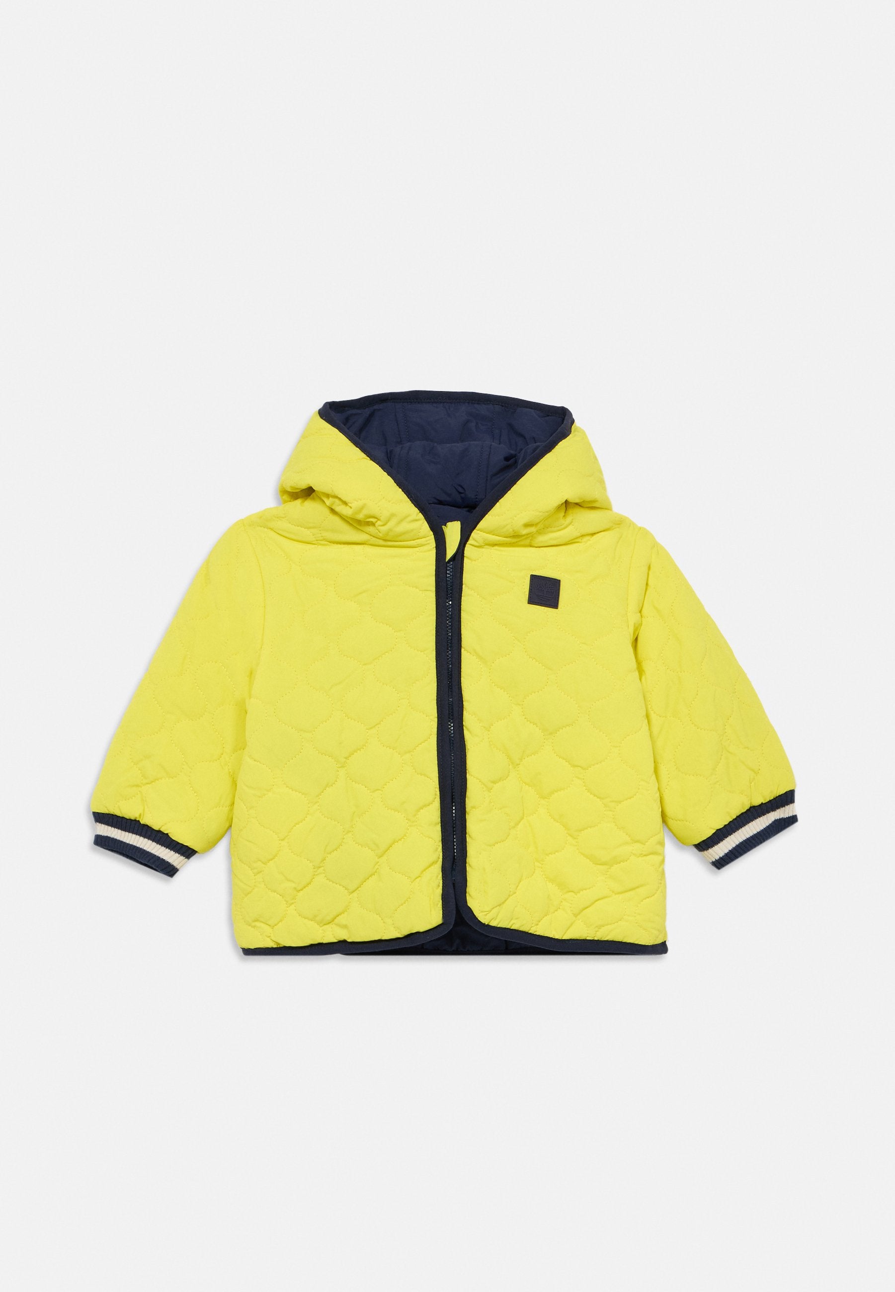 Gesteppte gelbe Jacke mit dunkelblauer Kapuze, vorne mit Reißverschluss und dunkelblauen, gerippten Bündchen mit weißen Akzenten. Kleines Logo auf der Brust.