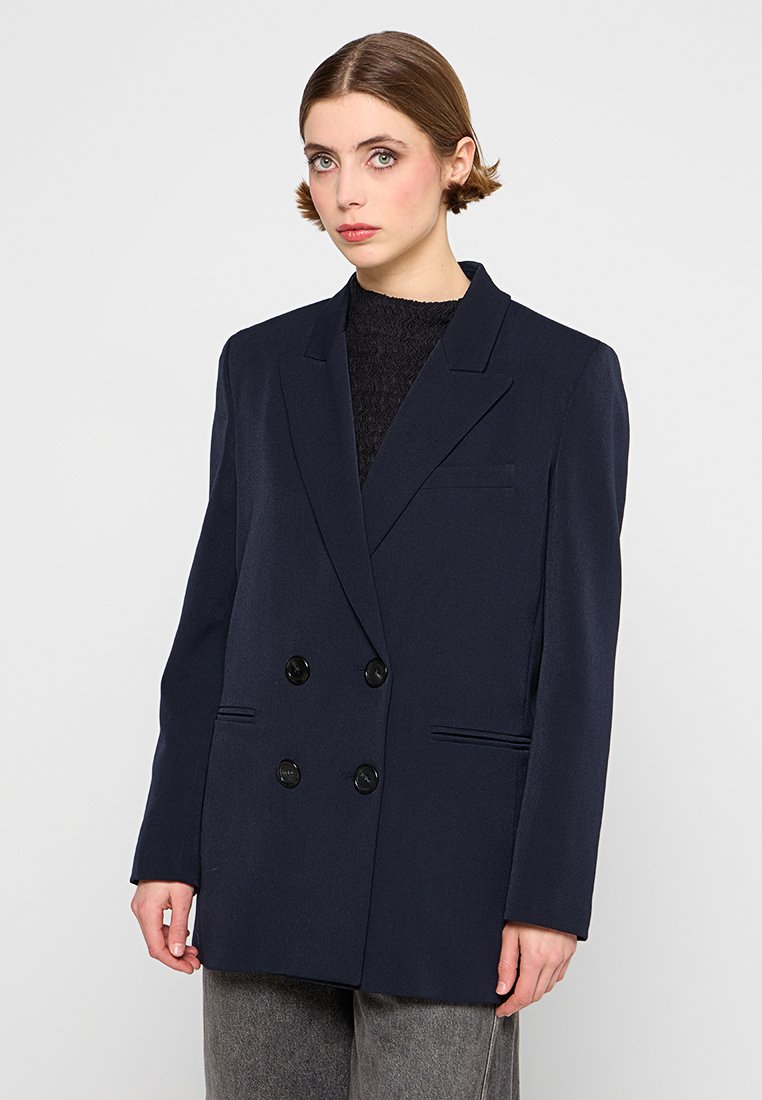 Marineblauer zweireihiger Blazer mit schwarzen Knöpfen, Revers und zwei Vordertaschen. Aus einem glatten, strukturierten Stoff gefertigt.