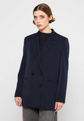 Marineblauer zweireihiger Blazer mit schwarzen Knöpfen, Revers und zwei Vordertaschen. Aus einem glatten, strukturierten Stoff gefertigt.