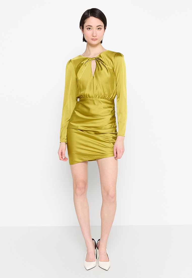 Knee-langes, olivgrünes Satin-Kleid mit langen Ärmeln, Schlüsselloch-Ausschnitt, gerafftem Bund und Rüschendetails, kombiniert mit weißen Heels.
