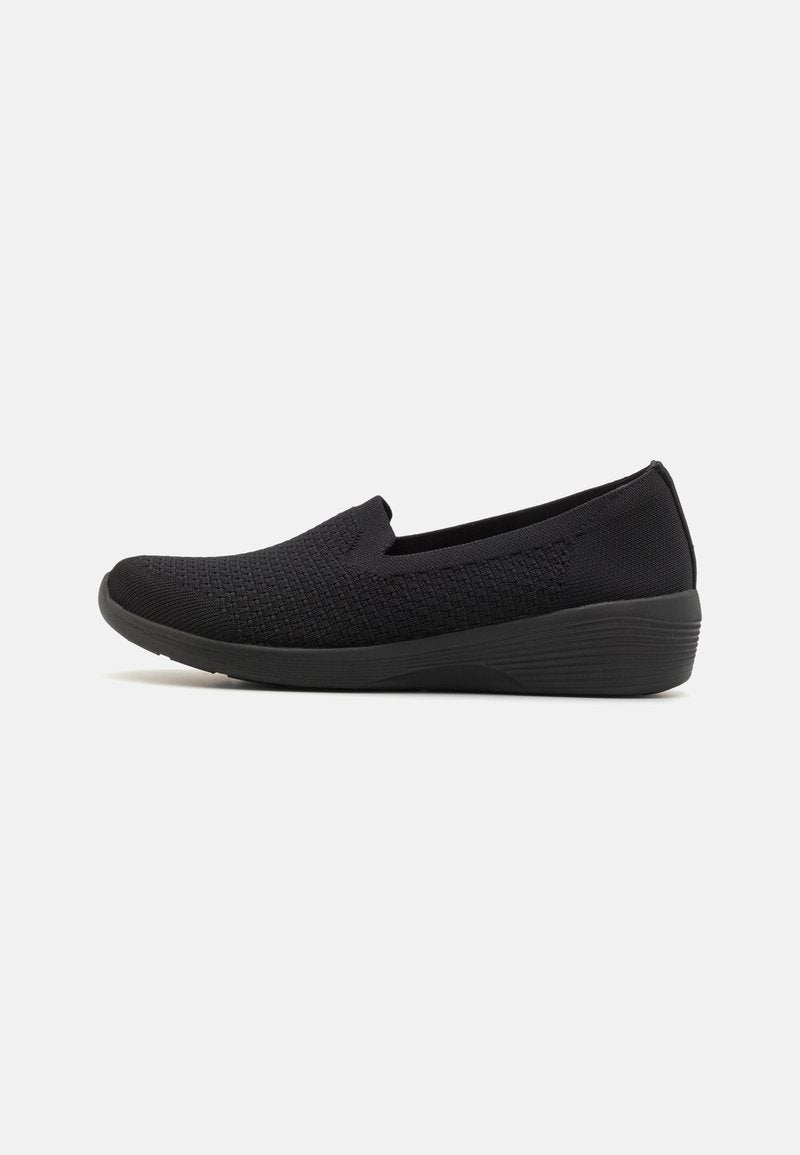 Schwarzer Slipper mit strukturiertem Obermaterial aus Strick und leicht erhöhter Sohle, entworfen für Freizeit- oder Komfortschuhe, seitlich auf weißem Hintergrund abgebildet.