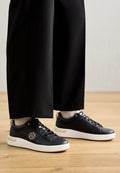 Schwarze Leder-Sneaker mit strukturiertem Finish, weißer Gummisohle und goldenen Akzenten. Die Schnürsenkel sind schwarz, mit einem runden Logo an der Seite.
