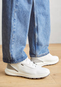 Weiße Sportschuhe mit strukturiertem Material und grauen Akzenten, kombiniert mit locker sitzenden blauen Jeans. Sichtbare Gummisohle und Schnürdetails.