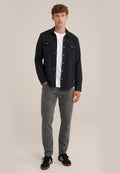 Schwarze Button-up-Hemd über einem weißen T-Shirt, graue Jeans und schwarze Sneakers. Das Hemd hat zwei Brusttaschen und silberne Knöpfe.