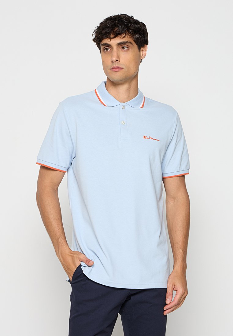 Helles blaues Poloshirt mit orangefarbenen Streifen am Kragen und an den Ärmelbündchen. Verfügt über eine zwei-Knopf-Leiste und ein gesticktes Logo auf der Brust.