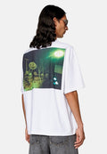 Weißes, übergroßes T-Shirt mit einem großen Grafikdruck auf der Rückseite, der eine dunkle, surreale Landschaft mit Bäumen und einem grünlichen Farbton darstellt.