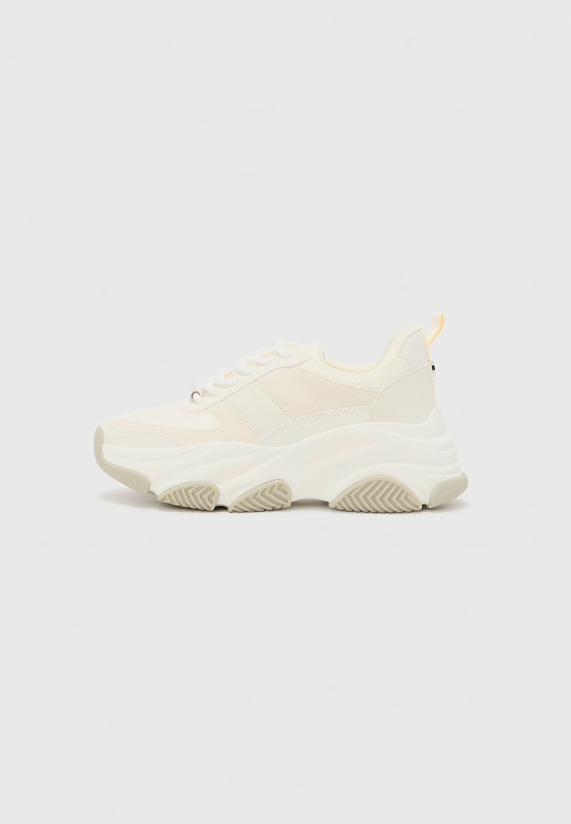 Dicke weiße Sneakers aus Mesh und synthetischen Materialien, mit strukturierten Akzenten, einer dicken Sohle und einem kleinen gelben Fersenlabel.