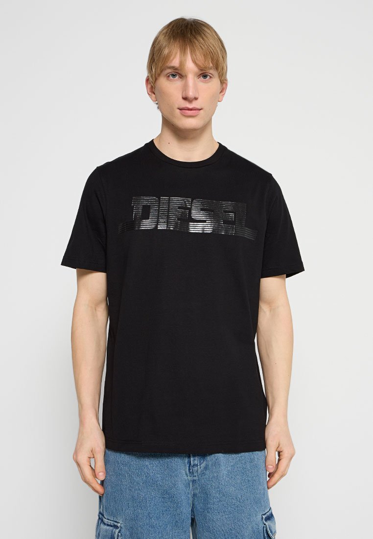 Schwarzes Baumwoll-T-Shirt mit einem horizontalen, reliefgeprägten "DIESEL"-Logo in glänzendem Schwarz. Kurze Ärmel, Rundhalsausschnitt, lockere Passform. Legere Denim-Shorts.