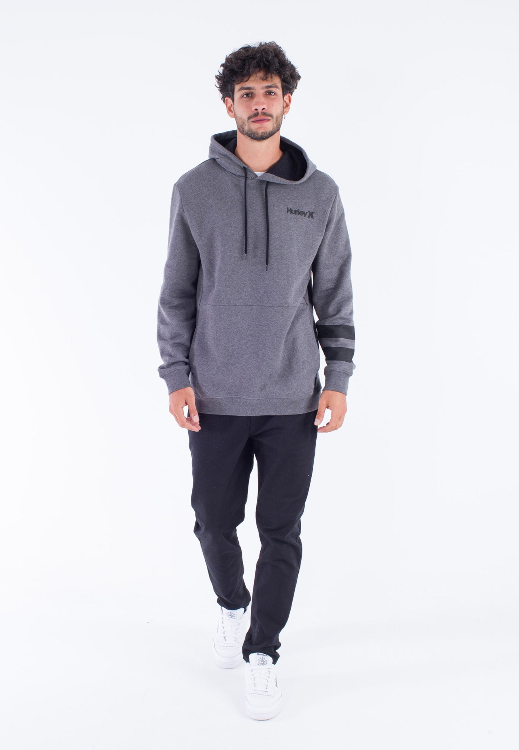 Grauer Kapuzenpullover mit schwarzen Akzenten und Kordeln. Verfügt über eine glatte Textur und ein gedrucktes Logo auf der Brust, kombiniert mit schwarzen Hosen und weißen Sneakers.