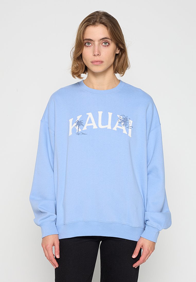 Hellblaues Sweatshirt mit Rundhalsausschnitt, das ein gedrucktes "KAUAI"-Logo und Palmen-Grafiken zeigt. Hergestellt aus weichem Stoff mit lockerer Passform.