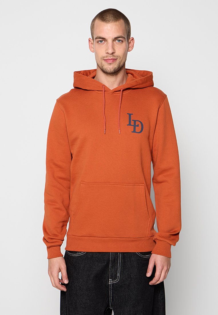 Oranger Pullover-Hoodie mit Fronttasche, Kapuze mit Kordelzug und marineblauem Logo auf der linken Brust. Hergestellt aus weichem, texturiertem Stoff.