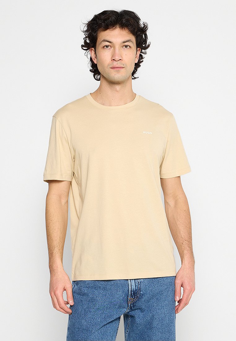 Beige Baumwoll-T-Shirt mit rundem Ausschnitt und kurzen Ärmeln. Kleiner weißer Logo-Schriftzug auf der linken Brustseite. Normale Passform.
