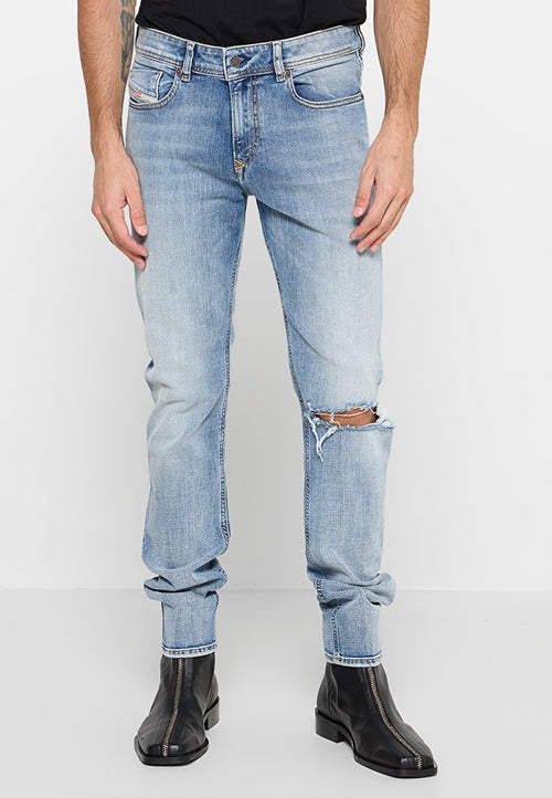 Hellblaue Jeans im Slim-Fit-Schnitt, mit distressed Knie-Öffnungen und einer leicht verwaschenen Textur. Kombiniert mit schwarzen Stiefeletten.