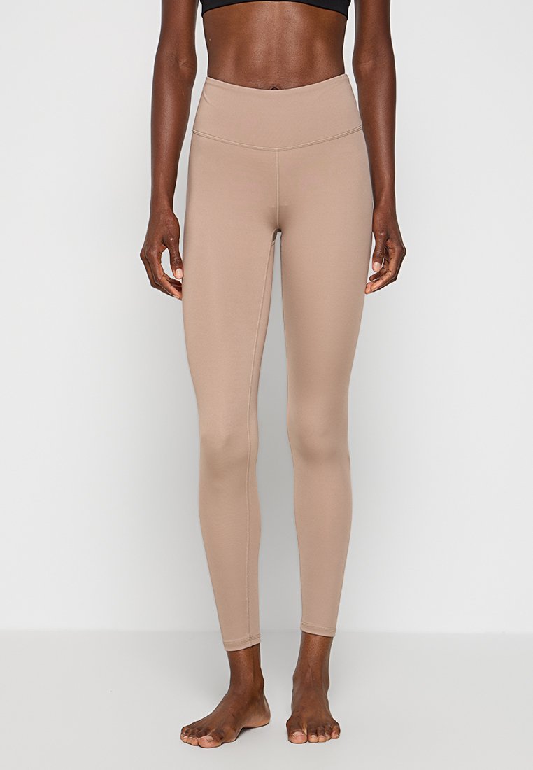 Beige Leggings mit hoher Taille aus elastischem Stoff, die eine glatte Textur und ein körperbetontes Design aufweisen und bis zu den Knöcheln reichen.
