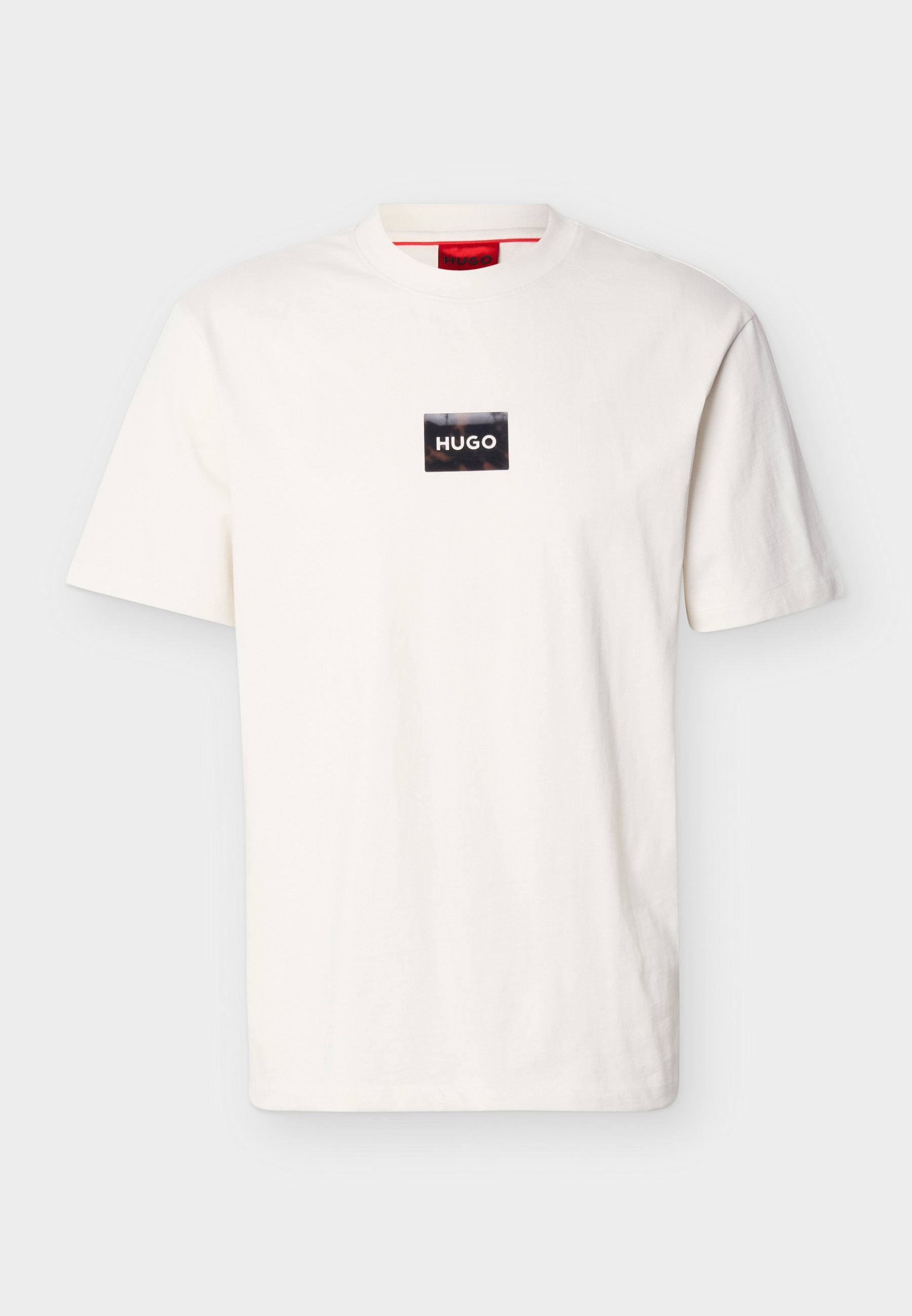Weißes T-Shirt mit kurzen Ärmeln und Rundhalsausschnitt, versehen mit einem kleinen schwarzen rechteckigen Aufnäher und weißem "HUGO"-Schriftzug auf der Brust.