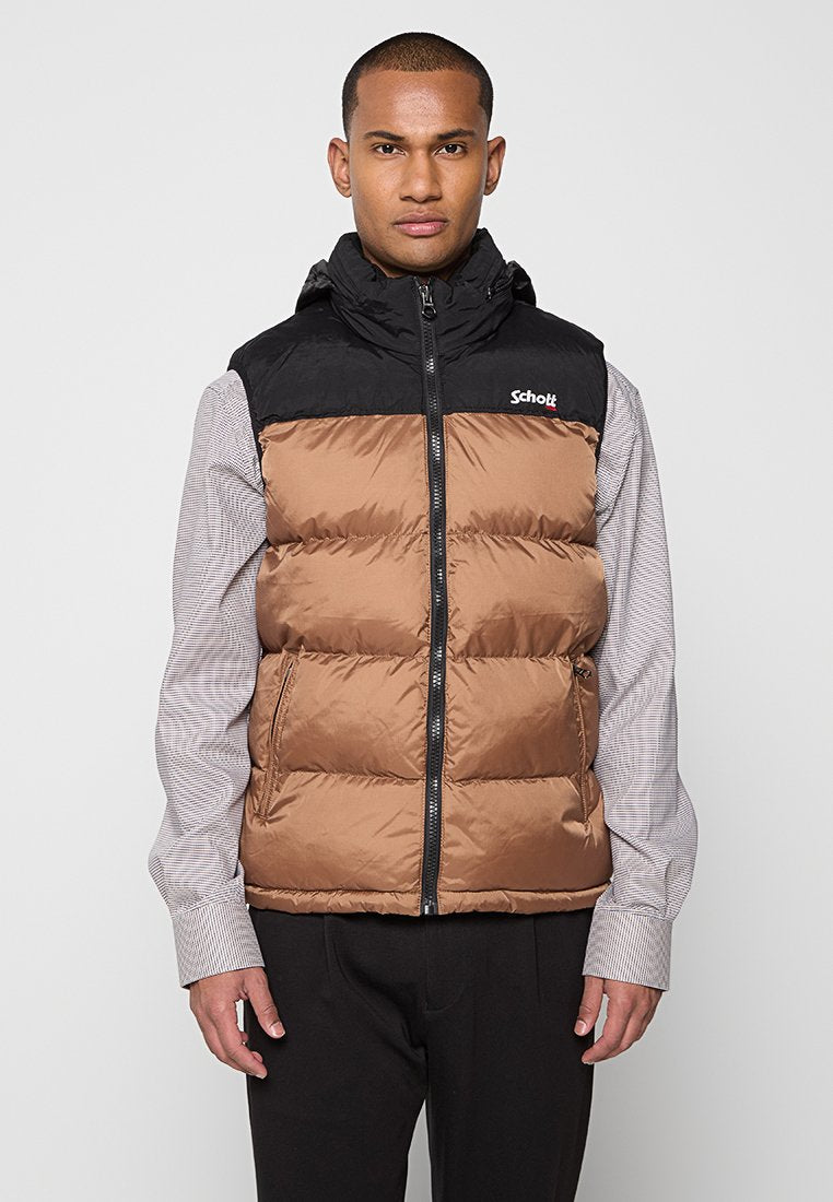 Weste aus Steppmaterial mit der oberen Hälfte aus schwarzem Nylon und der unteren Hälfte in braunem Steppmuster. Mit einem Reißverschluss und einem Logo auf der Brust. Getragen über einem gestreiften Hemd.