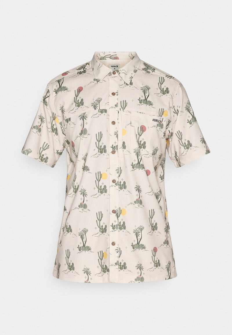 Kurzarmshirt aus beigem Stoff mit einem Muster aus Kakteen und Sonne. Verfügt über einen Kragen, Knöpfe und eine Brusttasche. Branding auf der Tasche.