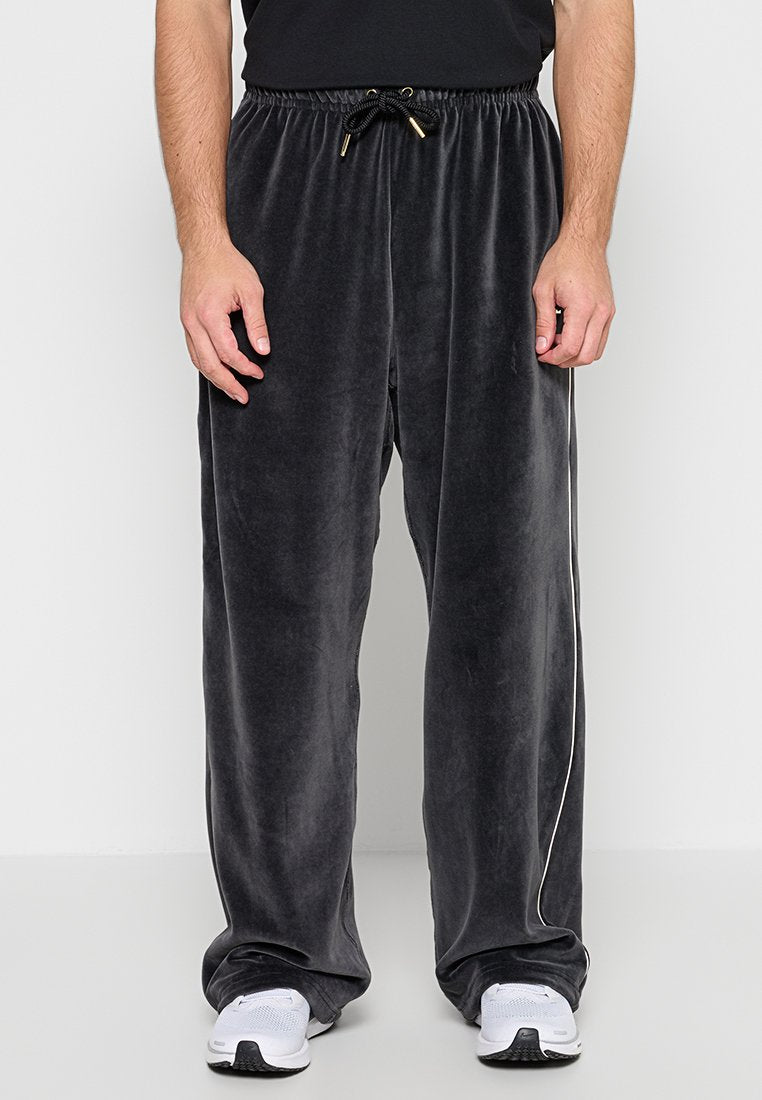 Schwarze lockere Velours-Hose mit elastischem Bund und Kordelzug, getragen mit weißen Sneakers und einem schwarzen Hemd.