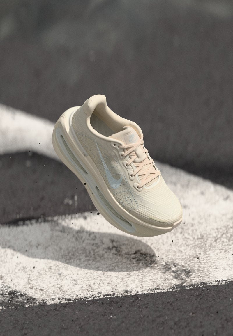Hellbeiger Sneaker mit strukturiertem Mesh-Obermaterial und einem zarten rosa Schnürsystem. Verfügt über ein markantes Nike-Swoosh-Logo und sichtbare Air-Dämpfung.