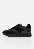 Schwarzer Sneaker mit niedrigem Schaft, Veloursleder- und glänzenden Einsätzen, Schnürverschluss und dicker Gummisohle, von der Außenseite gezeigt.