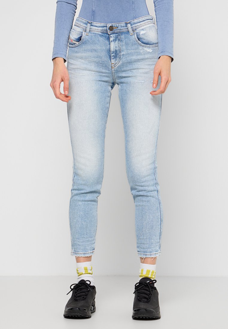Hellblaue Jeans im Slim-Fit-Stil mit fransigem Saum und subtilen Verwaschungen. Getragen mit schwarzen Sportschuhen und gemusterten weißen Socken.