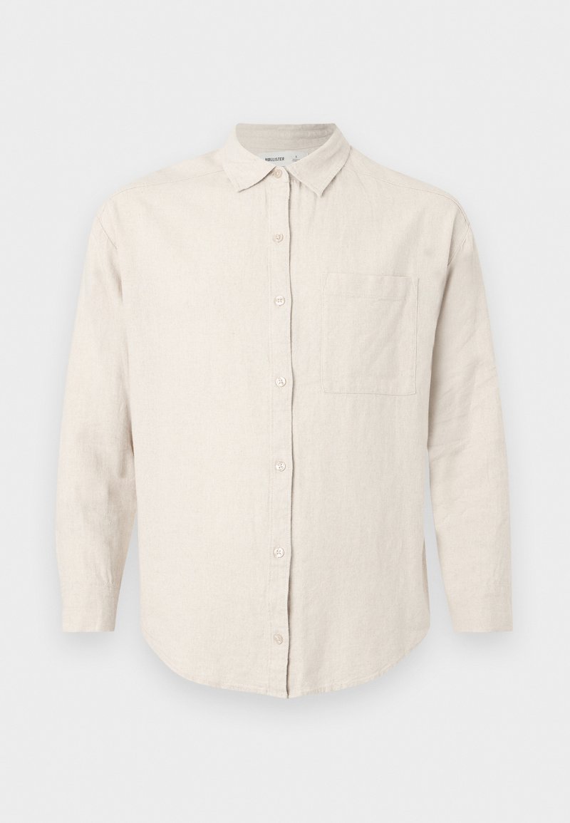 Beige langärmliges Hemd mit Knopfleiste, Kragen und Brusttasche, aus strukturiertem Stoff, auf weißem Hintergrund dargestellt.